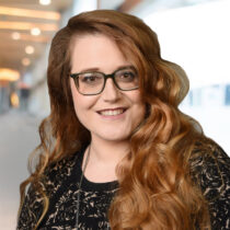 Molly Horak headshot in black dress with a fancy background.